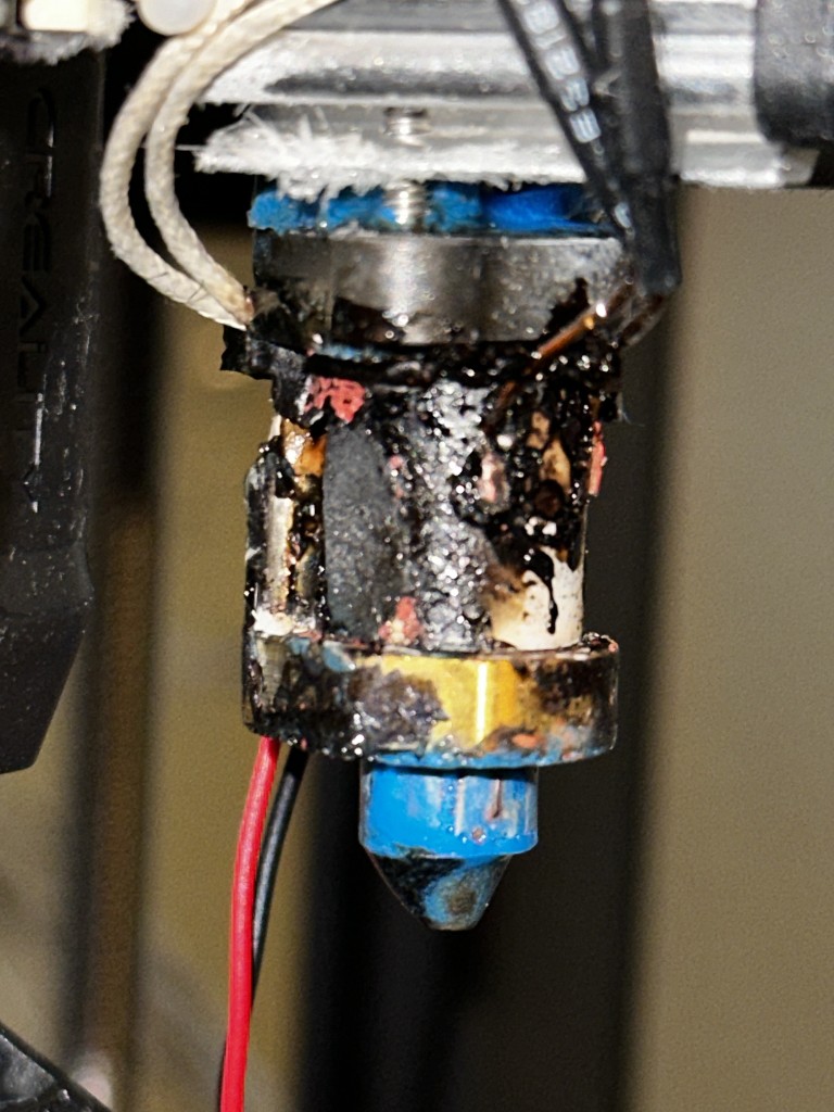 Schwer verstopftes Hotend mit verbranntem Filament um Düse und Heizblock